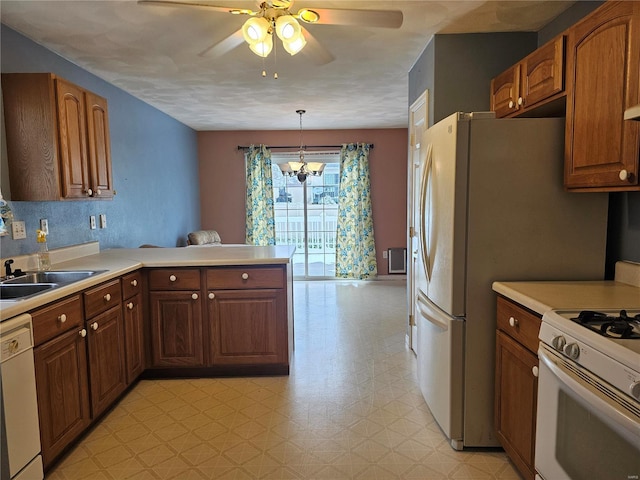 kitchen with white appliances, ceiling fan with notable chandelier, sink, decorative light fixtures, and kitchen peninsula