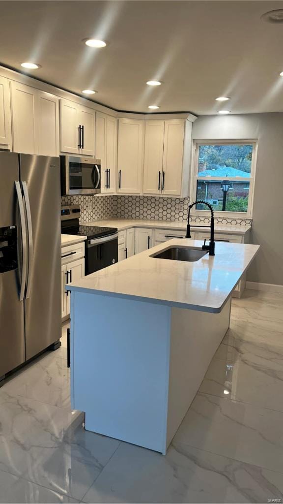 kitchen with backsplash, white cabinets, sink, an island with sink, and stainless steel appliances