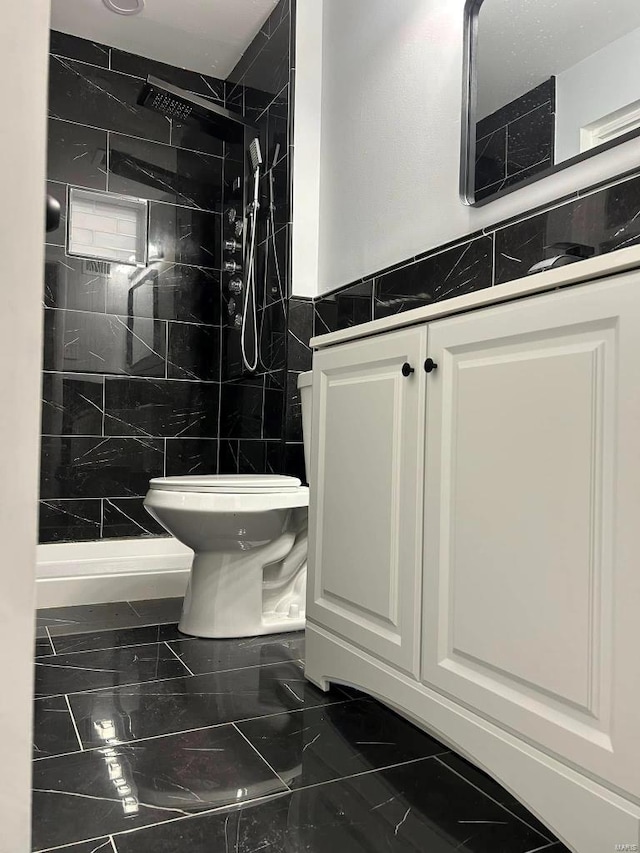 bathroom featuring a tile shower, vanity, toilet, and tile walls