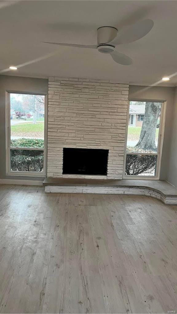 unfurnished living room featuring ceiling fan, a fireplace, and light wood-type flooring