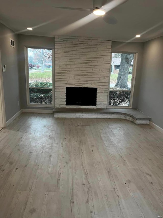 unfurnished living room with ceiling fan, a fireplace, a healthy amount of sunlight, and light hardwood / wood-style floors