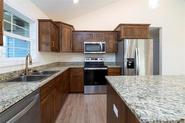 kitchen featuring sink, light hardwood / wood-style flooring, vaulted ceiling, light stone countertops, and appliances with stainless steel finishes