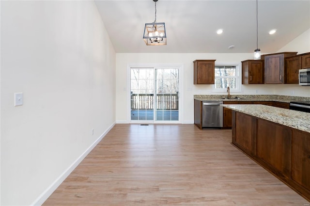 kitchen with light stone counters, pendant lighting, stainless steel appliances, and light hardwood / wood-style floors