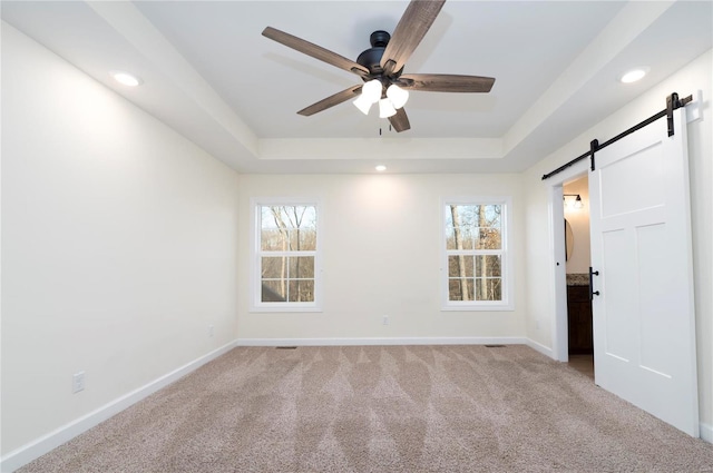 carpeted empty room featuring plenty of natural light, a barn door, and a raised ceiling