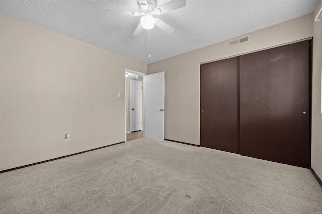 unfurnished bedroom featuring ceiling fan, a closet, light colored carpet, and a textured ceiling