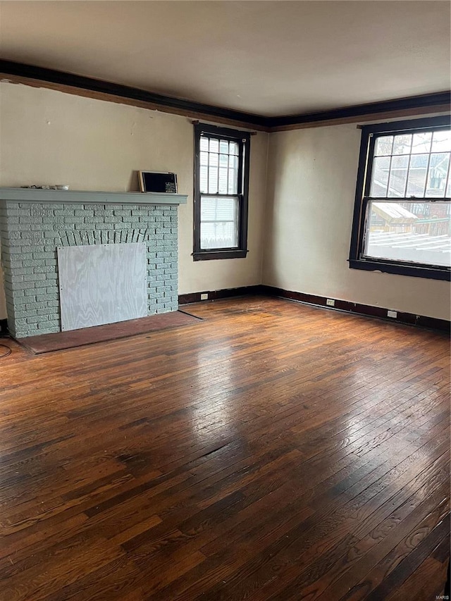 unfurnished living room featuring a wealth of natural light, ornamental molding, dark wood-type flooring, and a brick fireplace