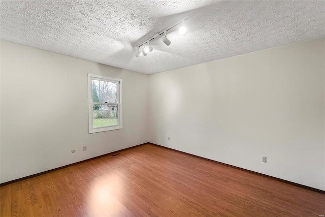 empty room with hardwood / wood-style floors, track lighting, and a textured ceiling