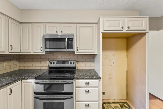 kitchen featuring appliances with stainless steel finishes, tasteful backsplash, dark stone counters, light hardwood / wood-style flooring, and white cabinetry