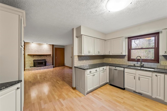 kitchen featuring white cabinets, sink, stainless steel dishwasher, light wood-type flooring, and a textured ceiling