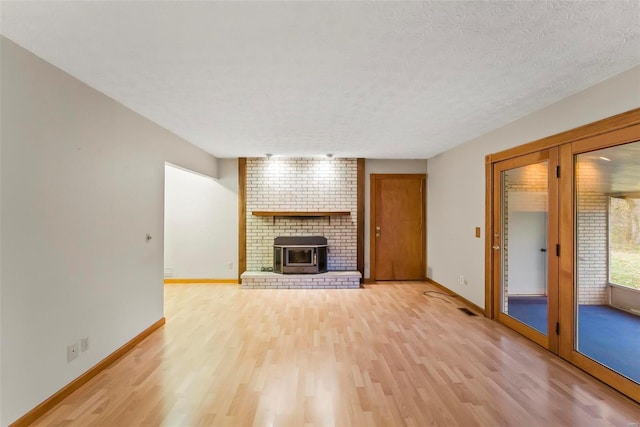 unfurnished living room with a wood stove, brick wall, a textured ceiling, and light wood-type flooring