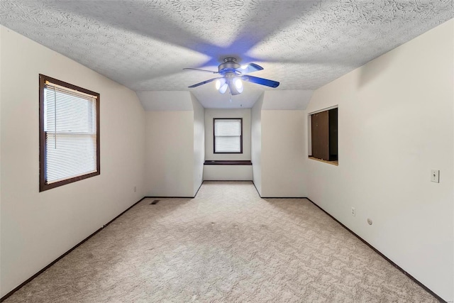 additional living space with a textured ceiling, plenty of natural light, light colored carpet, and lofted ceiling