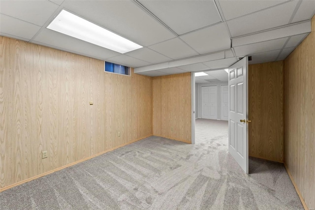 basement featuring a drop ceiling, light carpet, and wooden walls