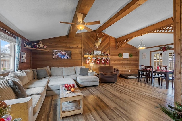 living room featuring ceiling fan, vaulted ceiling with beams, wood walls, hardwood / wood-style floors, and a textured ceiling