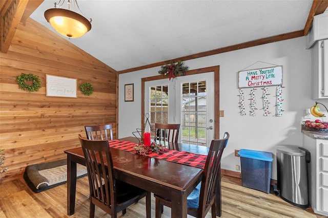 dining area featuring vaulted ceiling, light hardwood / wood-style flooring, wooden walls, and crown molding