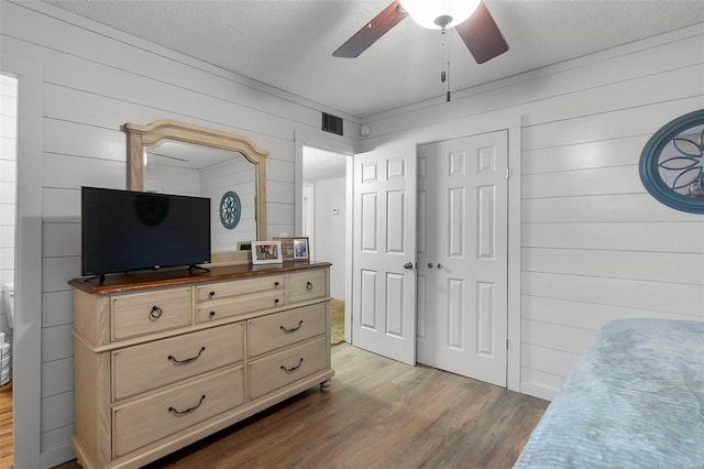 bedroom with ceiling fan, wooden walls, dark wood-type flooring, and a textured ceiling