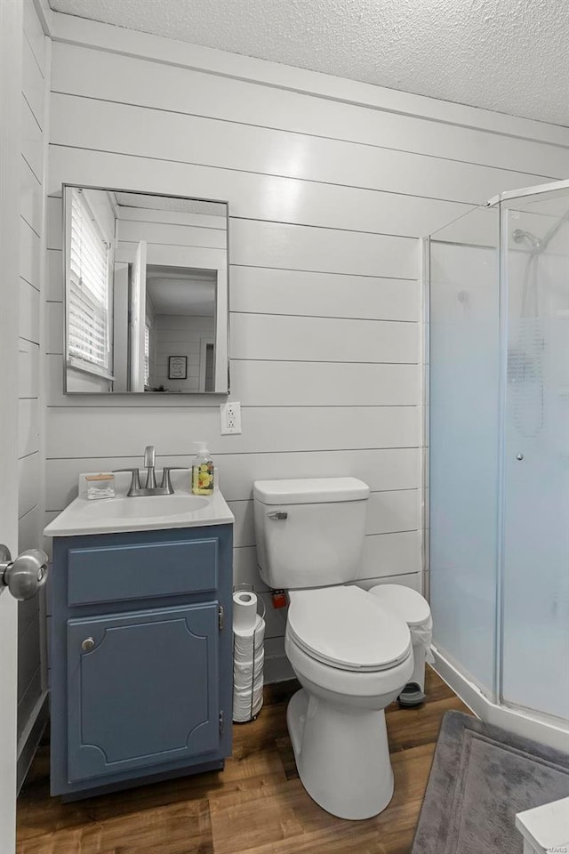 bathroom with vanity, a textured ceiling, wooden walls, hardwood / wood-style flooring, and a shower with shower door