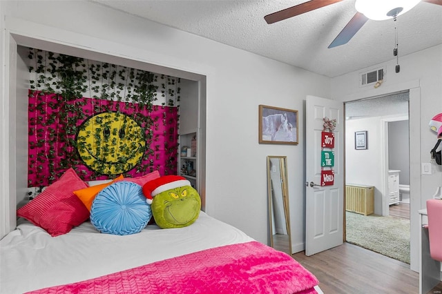 bedroom with a textured ceiling, light wood-type flooring, ensuite bathroom, and ceiling fan