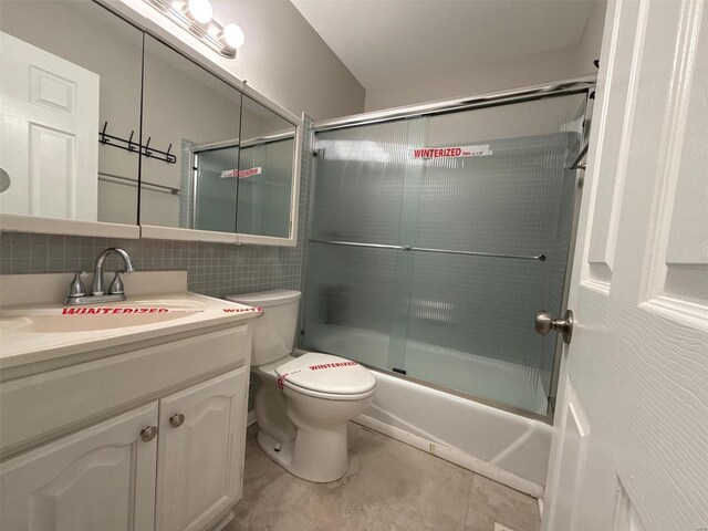 full bathroom featuring combined bath / shower with glass door, vanity, tile walls, tile patterned flooring, and toilet