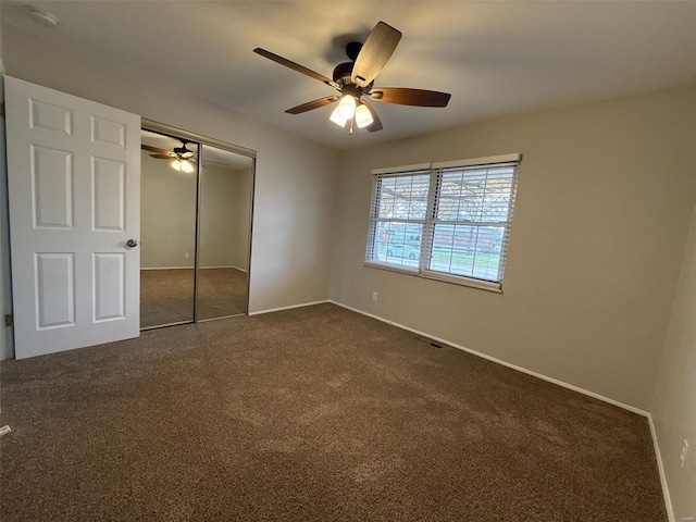 unfurnished bedroom featuring ceiling fan, dark carpet, and a closet