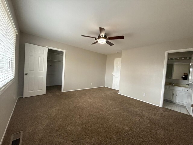 unfurnished bedroom featuring dark colored carpet, ensuite bath, and ceiling fan