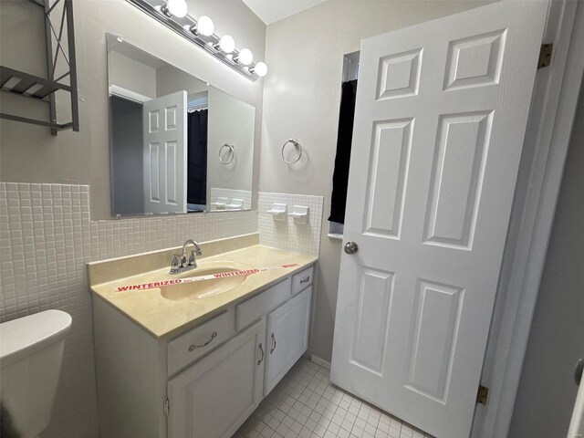 bathroom with tile patterned flooring, vanity, toilet, and tile walls