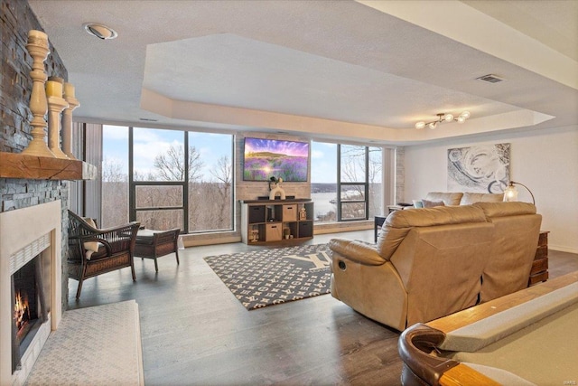 living room featuring a stone fireplace, wood-type flooring, a textured ceiling, and a tray ceiling