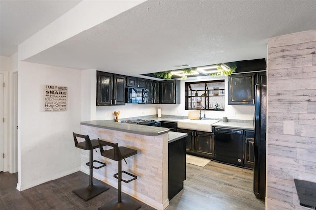 kitchen with wood walls, black appliances, sink, kitchen peninsula, and a breakfast bar area