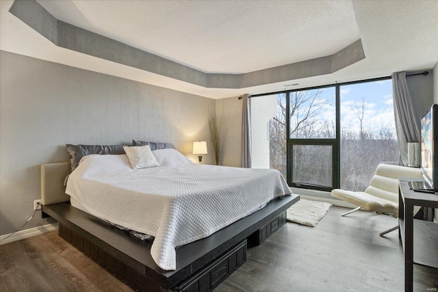 bedroom with hardwood / wood-style floors, a tray ceiling, and expansive windows