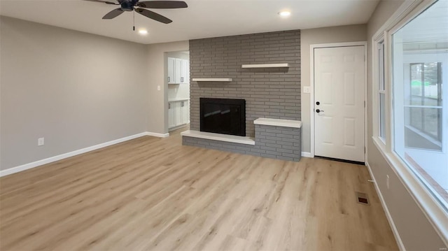 unfurnished living room with a brick fireplace, ceiling fan, and light hardwood / wood-style flooring