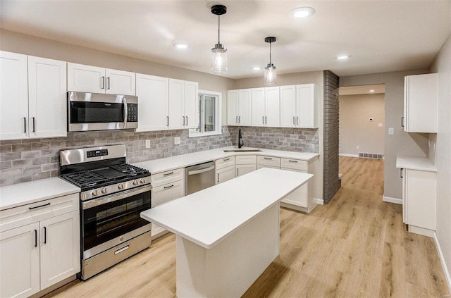 kitchen with white cabinets, sink, light wood-type flooring, appliances with stainless steel finishes, and a kitchen island