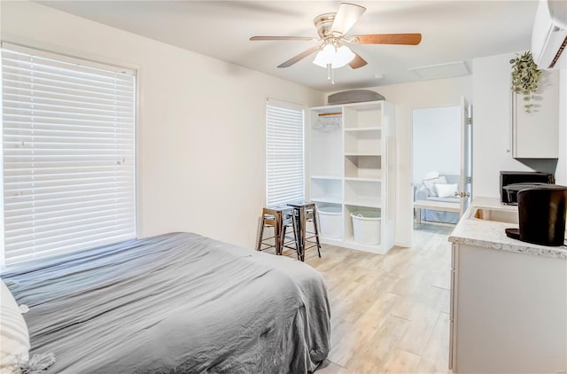 bedroom featuring a wall mounted AC, light hardwood / wood-style flooring, and ceiling fan