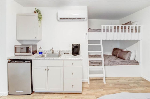 kitchen with a wall mounted air conditioner, appliances with stainless steel finishes, sink, light hardwood / wood-style flooring, and white cabinets