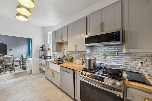 kitchen featuring wood counters, backsplash, a textured ceiling, gray cabinets, and appliances with stainless steel finishes