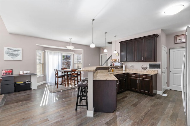 kitchen featuring a kitchen bar, light stone countertops, kitchen peninsula, dark wood-type flooring, and hanging light fixtures