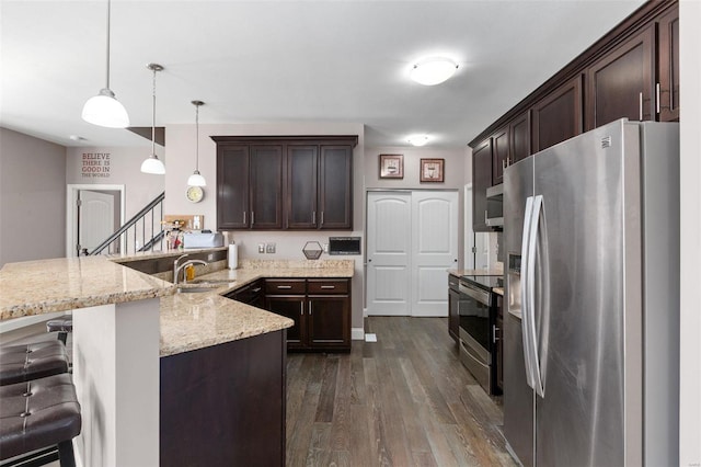 kitchen featuring dark wood-type flooring, hanging light fixtures, appliances with stainless steel finishes, a kitchen bar, and kitchen peninsula