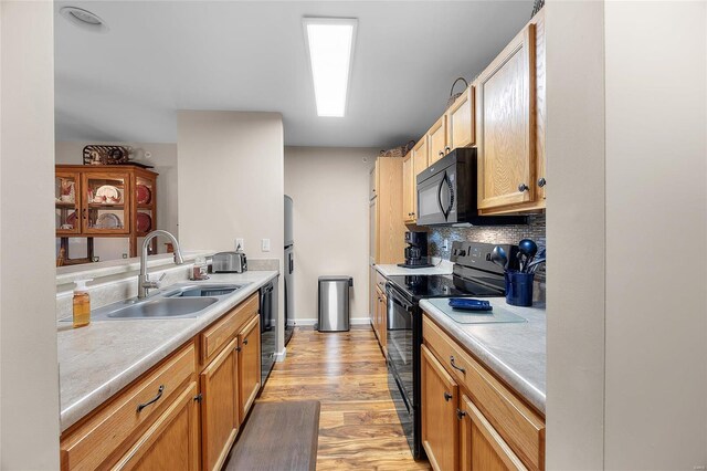 kitchen with tasteful backsplash, sink, black appliances, and light hardwood / wood-style flooring