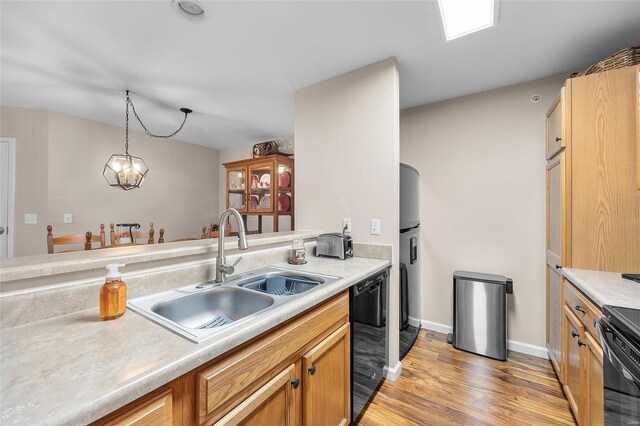 kitchen with black appliances, sink, hanging light fixtures, light hardwood / wood-style flooring, and a notable chandelier