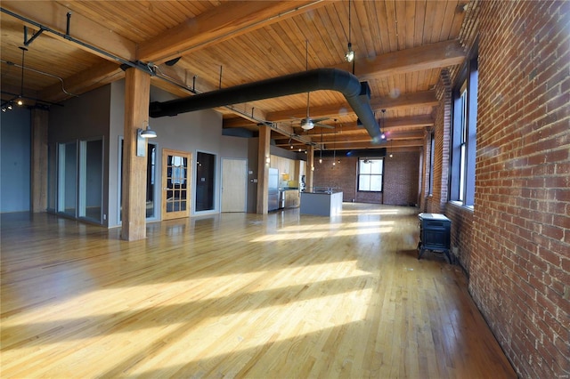 interior space with wooden ceiling, a high ceiling, beamed ceiling, light hardwood / wood-style floors, and brick wall