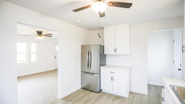 kitchen with light wood-type flooring, ceiling fan, sink, white cabinets, and stainless steel refrigerator