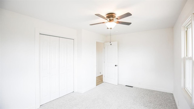 unfurnished bedroom featuring multiple windows, ceiling fan, a closet, and light carpet