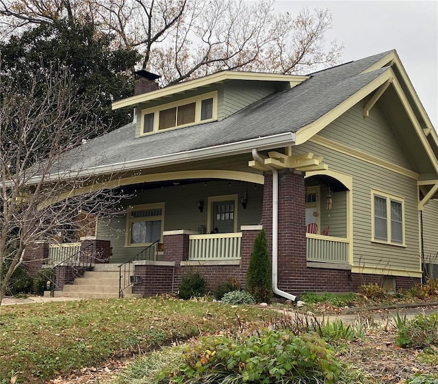 view of front of house with a shingled roof, covered porch, and a chimney