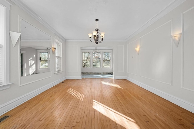 unfurnished dining area with a wealth of natural light, ornamental molding, a chandelier, and light wood-type flooring