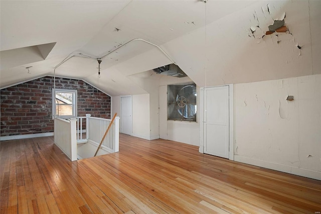 additional living space with brick wall, lofted ceiling, and hardwood / wood-style floors