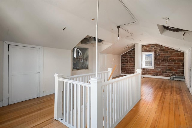 additional living space featuring vaulted ceiling, brick wall, and light hardwood / wood-style floors