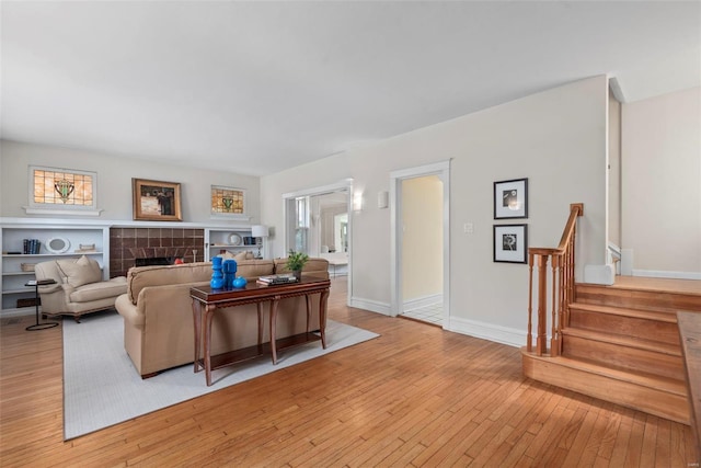 living area featuring stairs, light wood-style flooring, a tile fireplace, and a healthy amount of sunlight