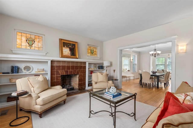living area featuring baseboards, a chandelier, visible vents, a fireplace, and wood finished floors