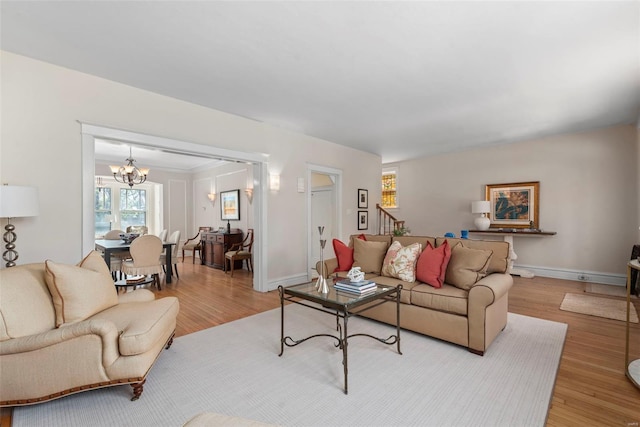 living room with baseboards, a notable chandelier, stairway, and light wood-type flooring