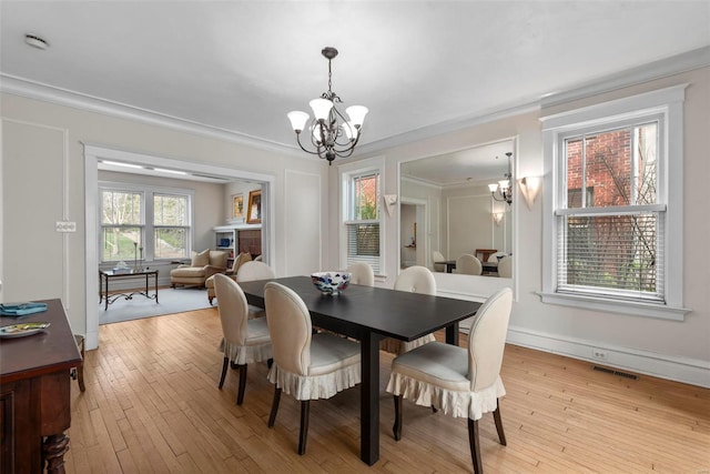 dining area featuring visible vents, light wood-style flooring, baseboards, ornamental molding, and an inviting chandelier