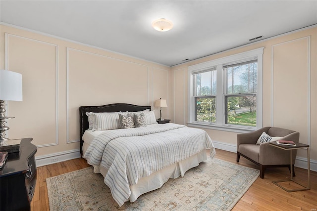 bedroom with light wood finished floors, baseboards, visible vents, and a decorative wall