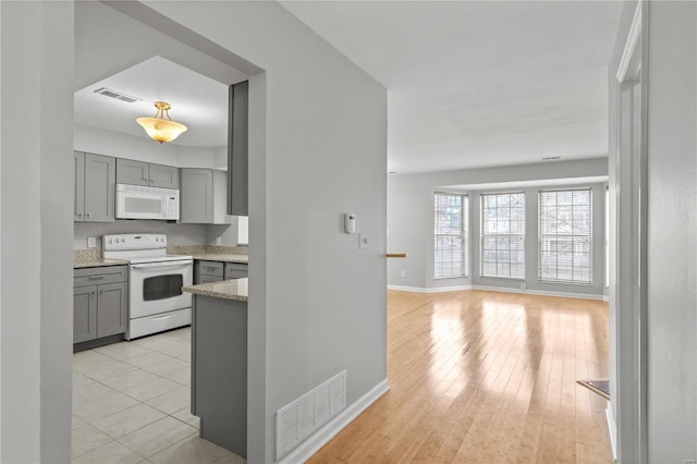 kitchen with gray cabinets, light stone counters, light hardwood / wood-style flooring, and white appliances